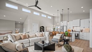 A spacious living room with a large sectional sofa, a coffee table, and a dining area with a kitchen in the background.