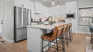 A modern kitchen with white cabinetry, stainless steel appliances, and a central island with bar stools.