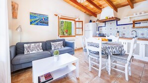 A cozy living area with a sofa, coffee table, and dining table. A kitchen with a tiled backsplash and wooden beams is visible.