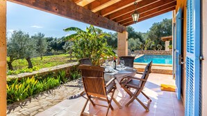 A covered patio with a pool, wooden chairs, and a table set for dining.