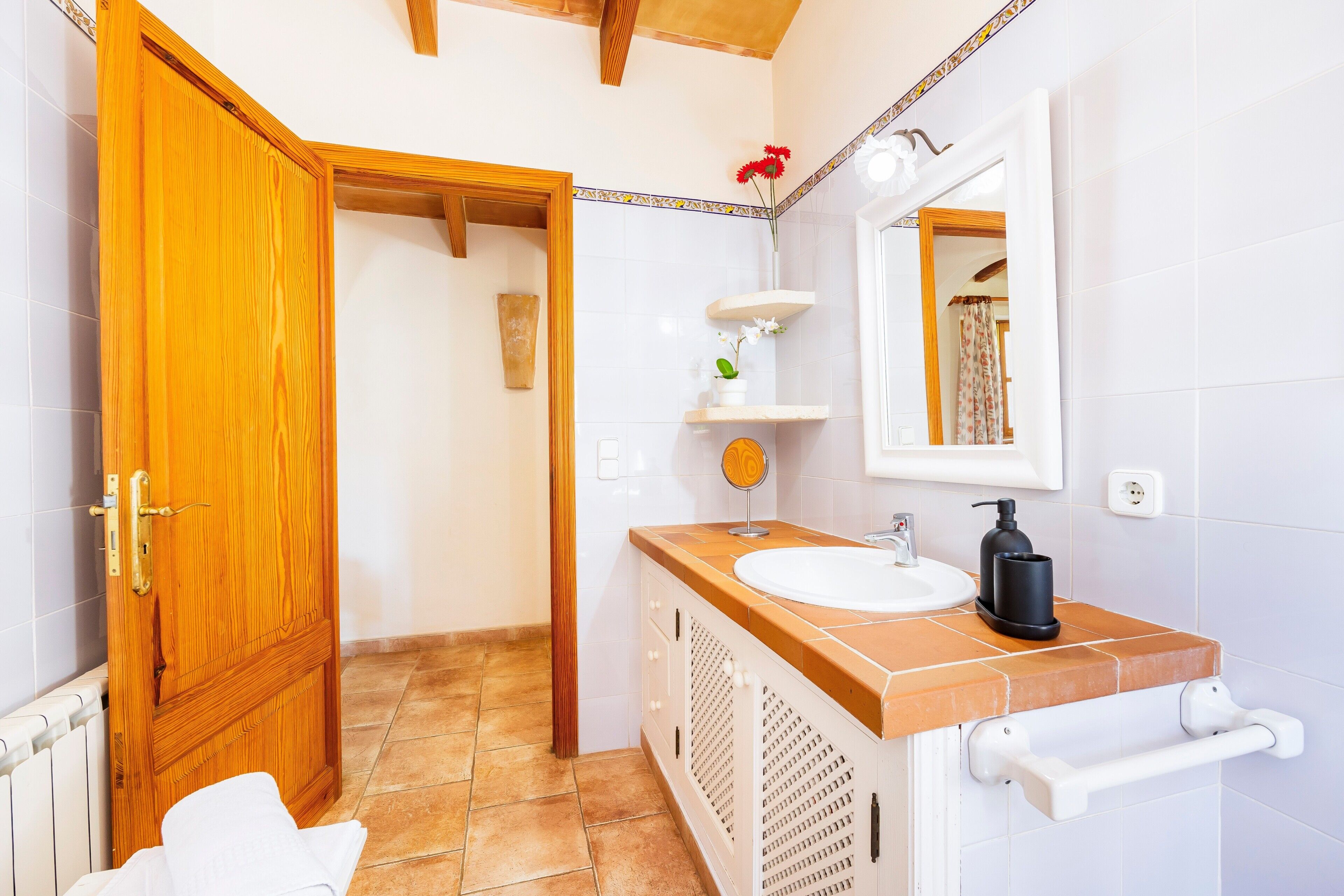 A bathroom with a wooden door, white tiles, a sink with a mirror, and a towel rack.