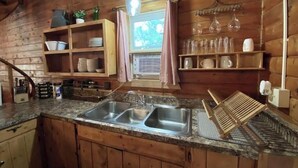 A wooden cabin kitchen with a granite countertop, double sink, and wooden cabinets.
