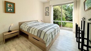 Un dormitorio con cama, mesita de noche, lámpara y un ventanal con vistas a zonas verdes.