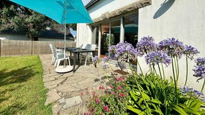 Un patio con una mesa, sillas, un paraguas azul y diversas flores.