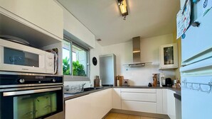 Una cocina moderna con gabinetes blancos, electrodomésticos de acero inoxidable y un ventanal que proporciona luz natural.