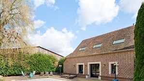 A brick building with a sloped roof, large windows, and a courtyard with outdoor seating. - Gîtes de France® - Domaine Majorelle (LA BELLIERE)