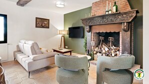 A living room with a fireplace, a sofa, two armchairs, a TV, and a painting on the wall. - Gîtes de France® - Domaine Majorelle (LA BELLIERE)