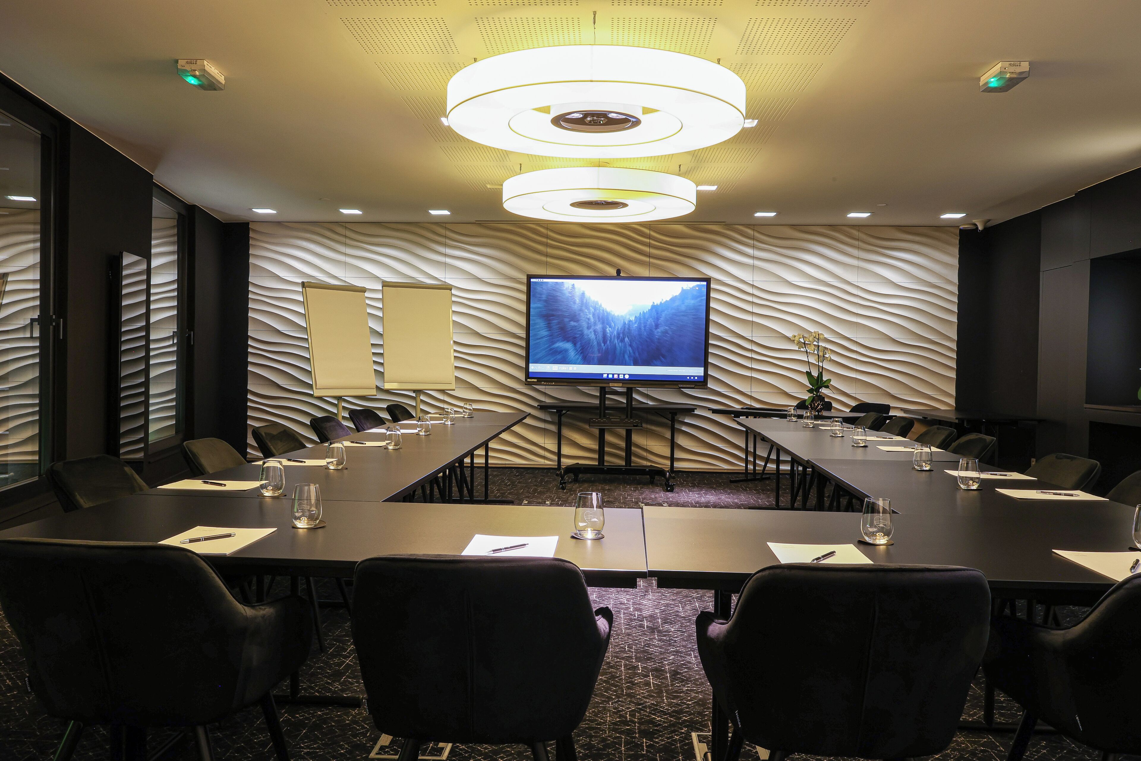 A conference room with a large table, chairs, a flat-screen TV, and a modern ceiling design.