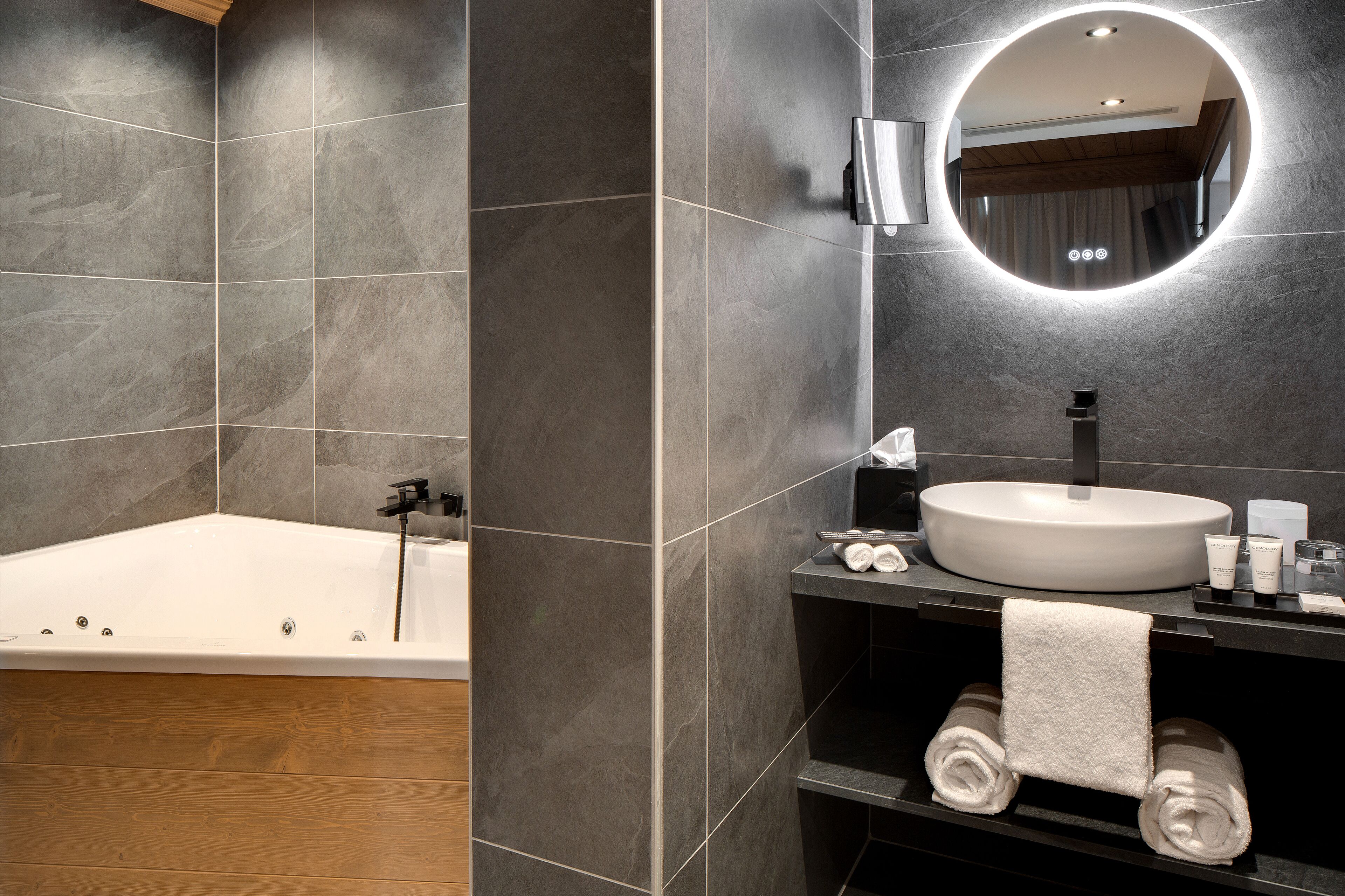 A modern bathroom with a freestanding bathtub, a round mirror with integrated lighting, and a vanity with toiletries.