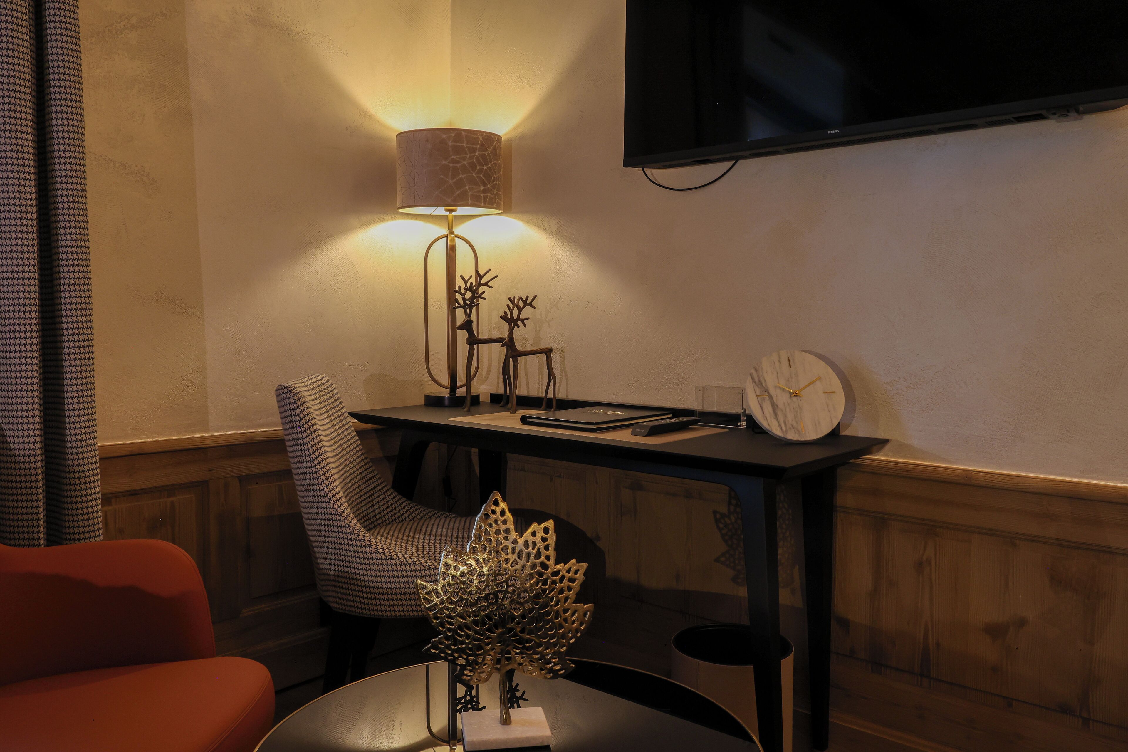 Une pièce chaleureuse avec un mur lambrissé en bois, une lampe moderne, une horloge et un téléviseur fixé au mur.