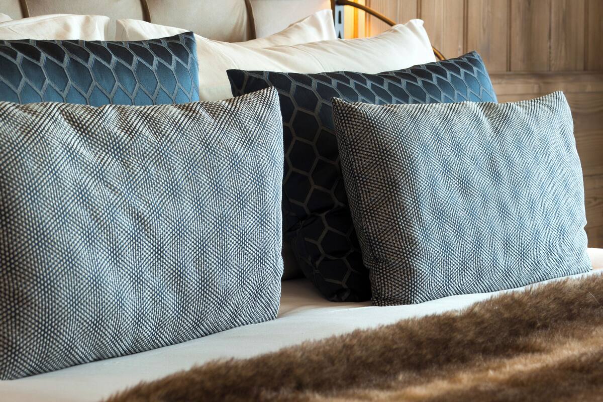 A bed with a tufted headboard, multiple pillows, a lamp, and a fur throw.