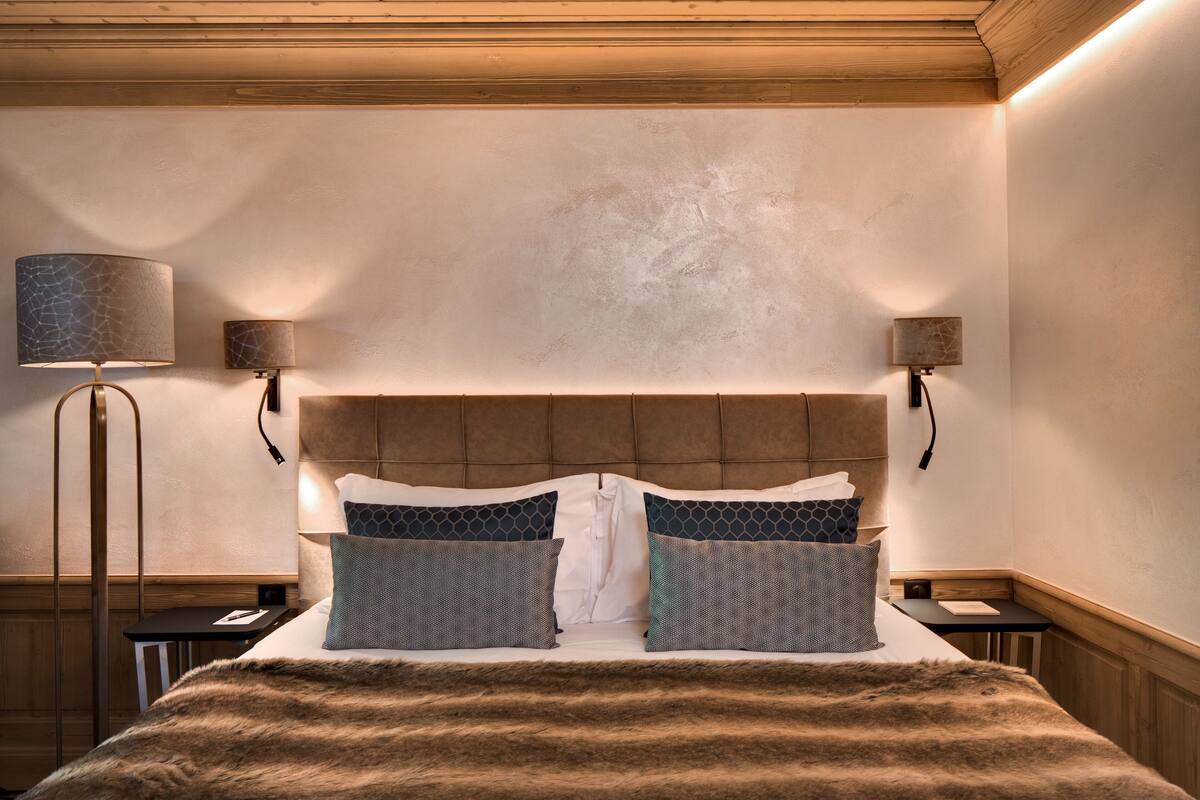 A neatly made bed with a fur throw, two bedside lamps, and a headboard with a textured pattern.