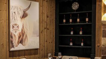 Un comedor con una mesa redonda, sillas, un cuadro grande enmarcado de una vaca y una estantería para vinos con botellas.
