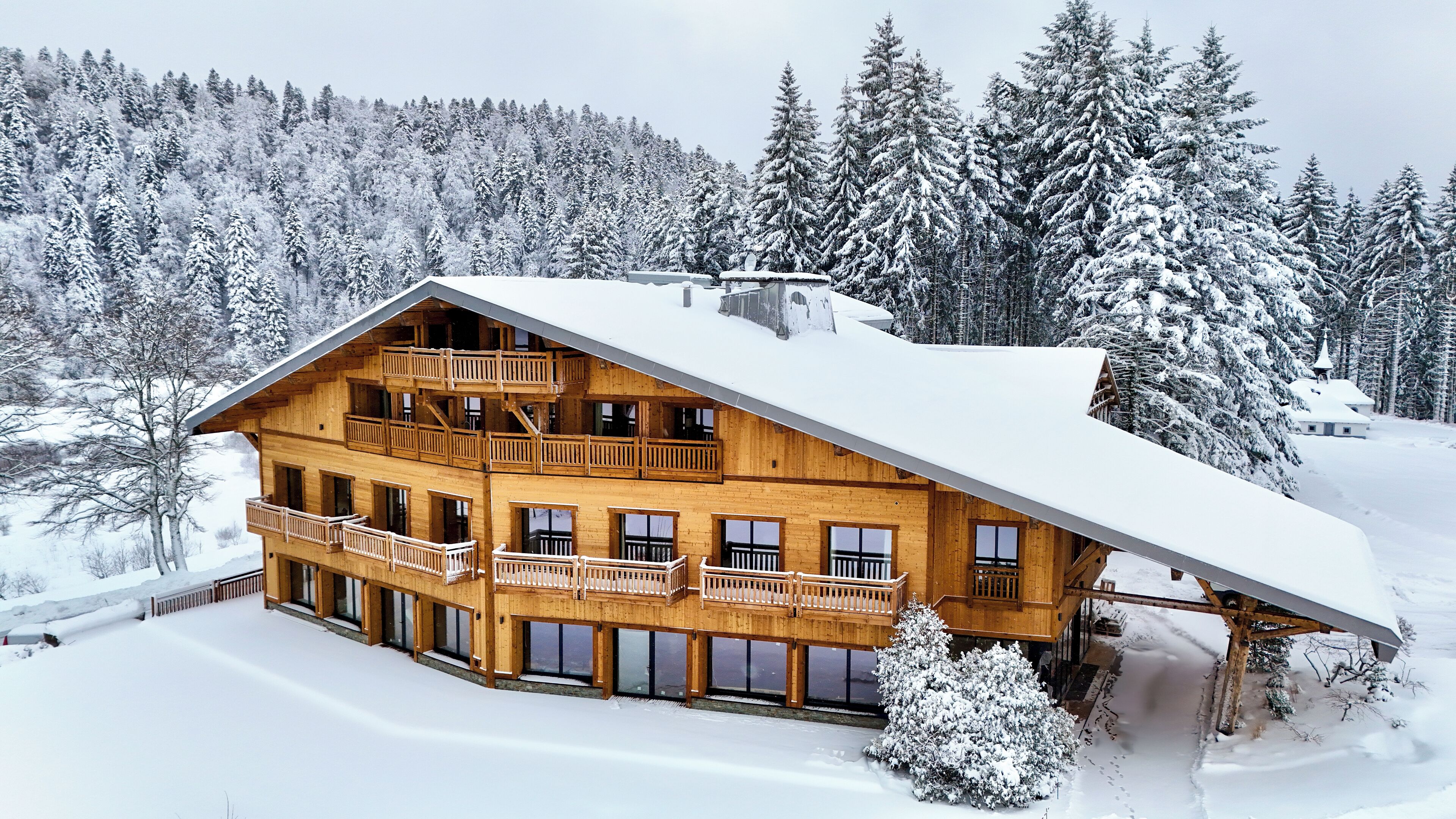 Een ruime houten chalet met meerdere balkons en een schuin dak, omringd door met sneeuw bedekte bomen.