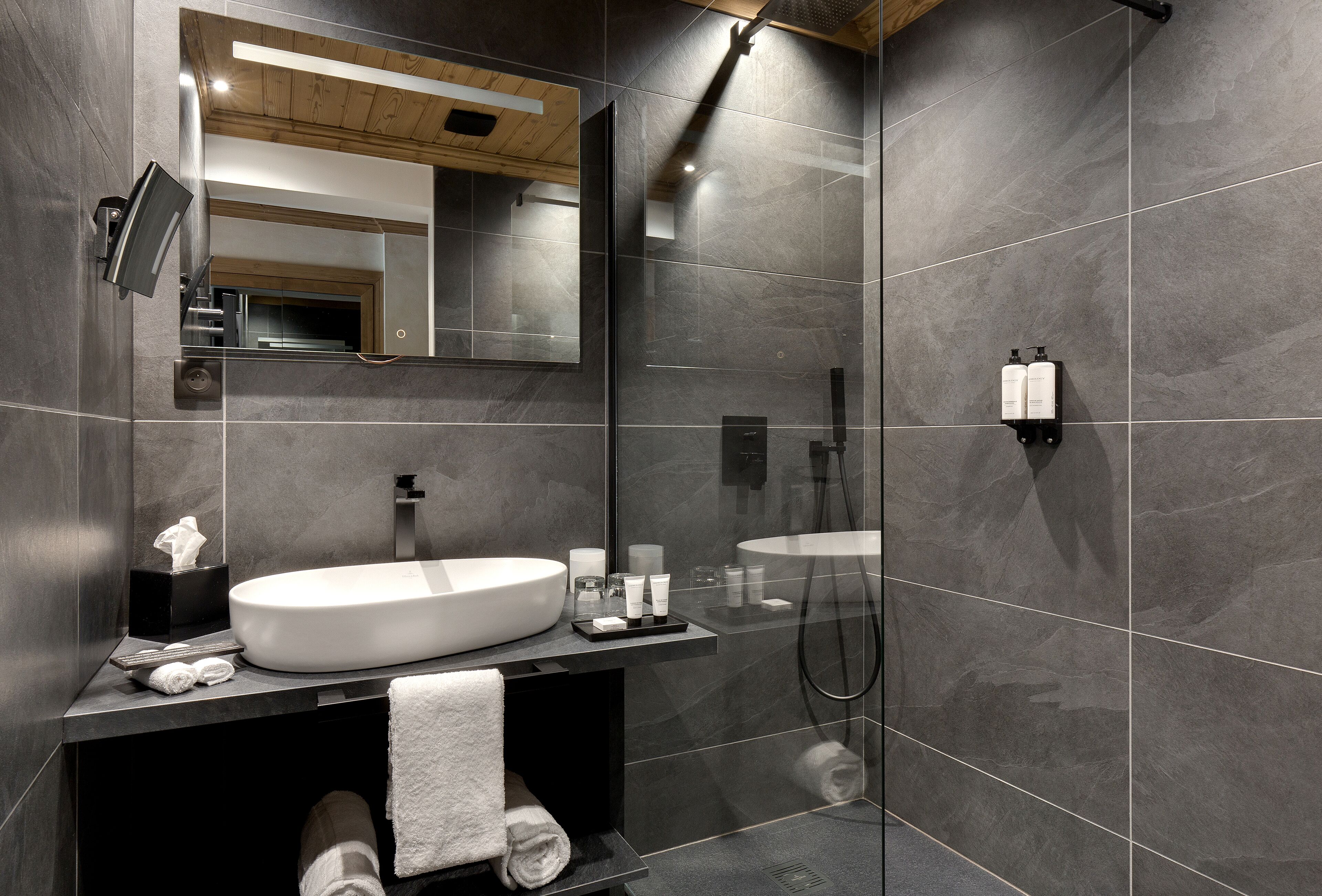 Un baño moderno con un espejo grande, un lavamanos blanco y una zona de ducha.