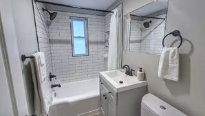 Un baño moderno con una bañera, un lavabo y un inodoro. Hay una ventana sobre la bañera y un espejo sobre el lavabo.
