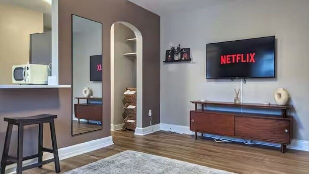 Una sala moderna con un televisor de pantalla plana montado en la pared, un mueble de madera y un espejo que refleja la habitación.