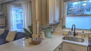 Cocina compacta con lavabo, armarios y ventana con vistas a árboles.