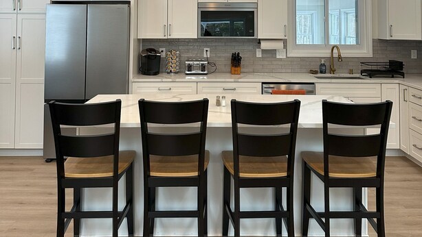 A modern kitchen with white cabinets, a stainless steel refrigerator, a central island with bar stools, pendant lighting, and a skylight. - Your Wolfeboro Home Away From Home (Wolfeboro)