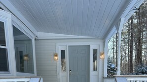A wooden porch with white railings and a gray door, surrounded by snow. - Your Wolfeboro Home Away From Home (Wolfeboro)
