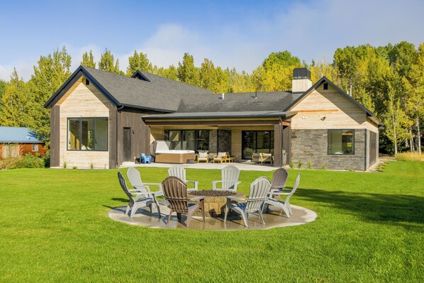 Ein modernes Haus mit einer Terrasse, die Gartenmöbel und eine Feuerstelle bietet.