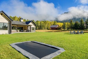 Ein modernes Haus mit einer großen Terrasse, einem Trampolin und Blick auf Berge und Bäume.