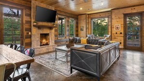 A cozy cabin interior with a stone fireplace, comfortable seating, and large windows offering natural light and views.