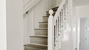 Un escalier avec des marches en bois et des rampes blanches, menant à une porte.