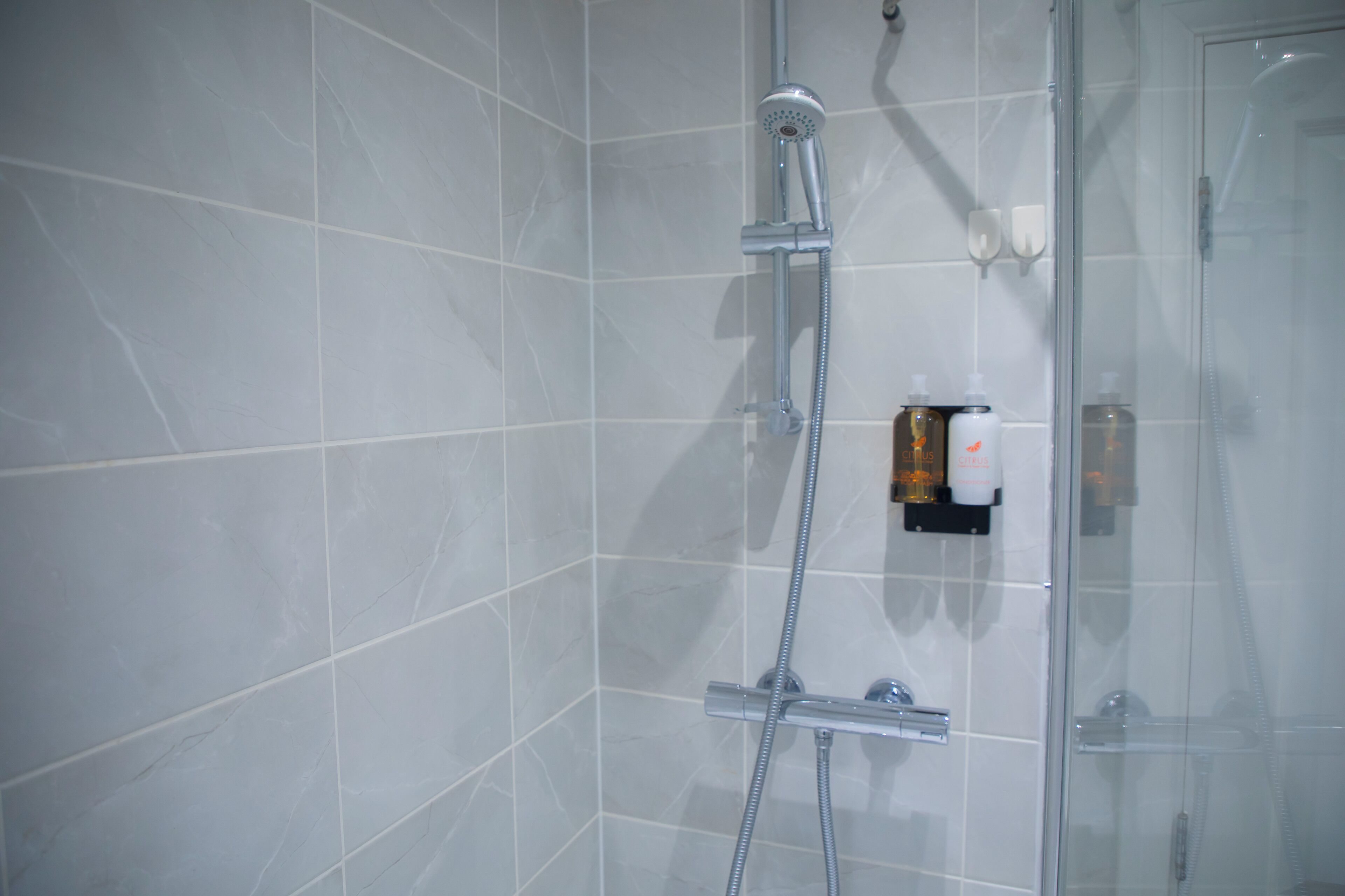 A shower area with a glass door, a handheld showerhead, and a soap dispenser on the wall.