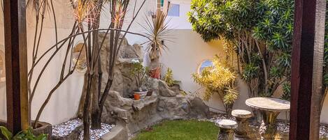 A covered patio area with a tiled floor, a small garden with rocks, plants, and a table.