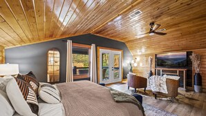A cozy bedroom with a large bed, a wooden ceiling, and a fireplace.