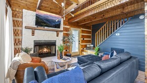 A cozy living room with a fireplace, a large sofa, and a staircase leading to an upper level.