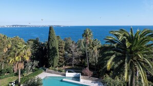 Ein Pool mit Blick auf das Meer, umgeben von Palmen und einer hohen Zypresse.