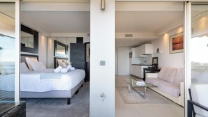Ein modernes Hotelzimmer mit einem großen Bett, einer separaten Wohnbereits mit einer Couch, einem Glastisch und Blick ins Freie.