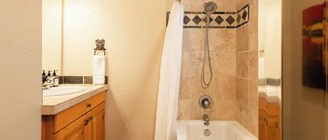 A bathroom with a bathtub, a shower, a sink, and wooden cabinets.