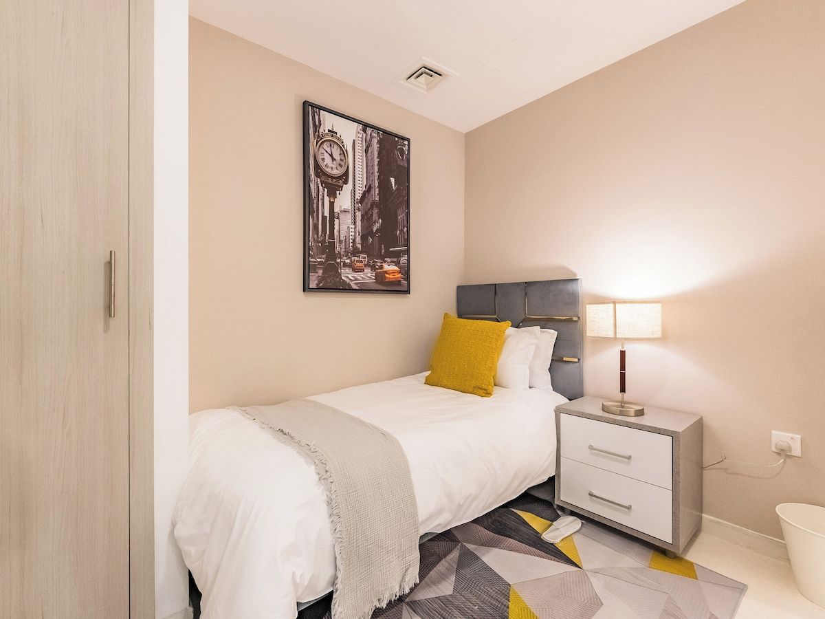 A bedroom with a bed, bedside table, lamp, and a framed picture on the wall.