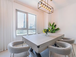 Een moderne eetkamer met een rechthoekige tafel, zes stoelen, een vaas met bloemen en een stadsgezicht door grote ramen.