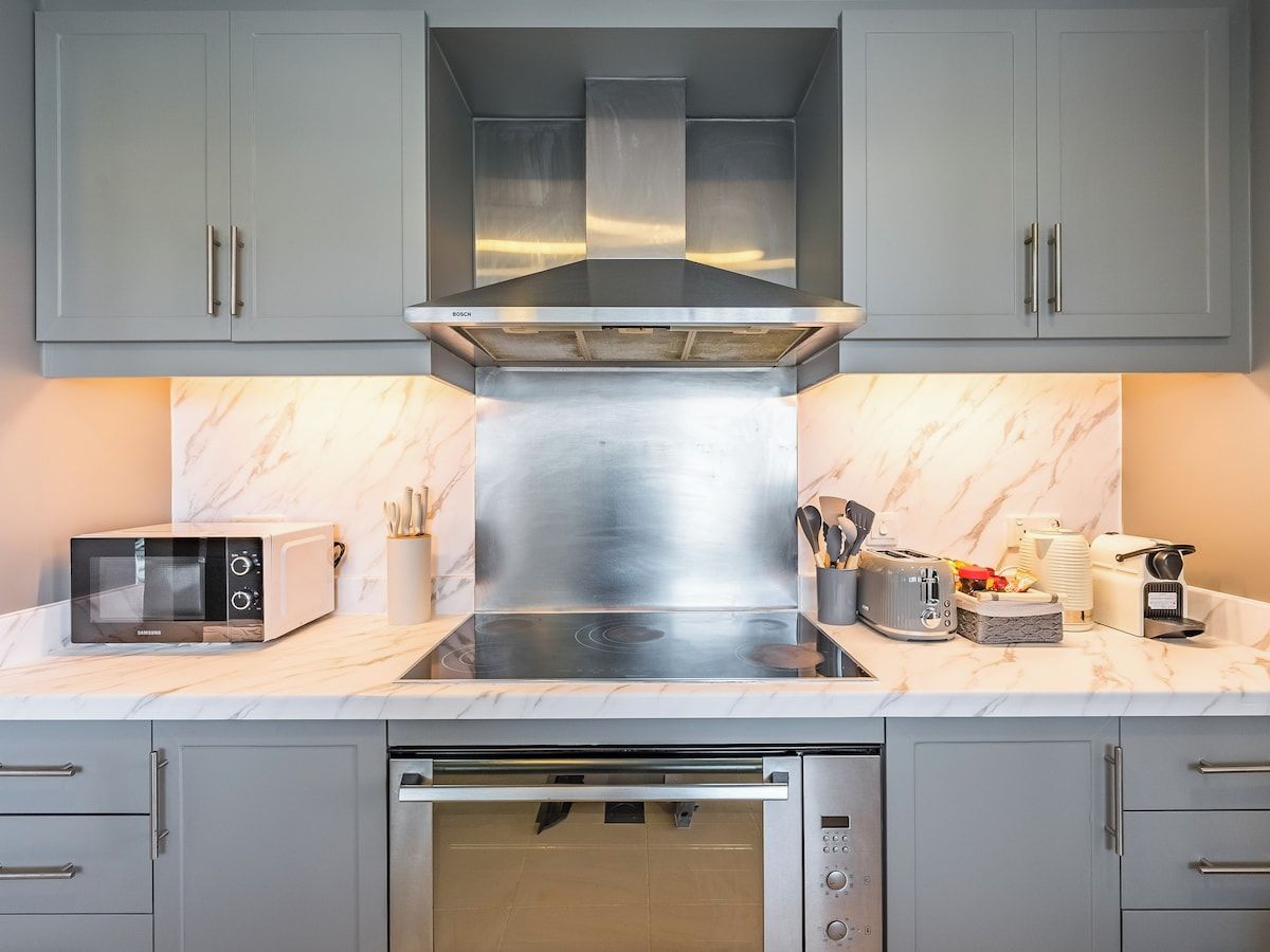 A modern kitchen with grey cabinets, a stainless steel range hood, a built-in oven, and a microwave.