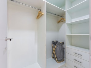 Un dressing accessible sans porte, doté d’étagères ouvertes, d’une tringle et d’un seul meuble à tiroir.