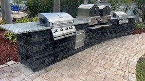 An outdoor kitchen with a built-in grill, a side burner, and a smoker, surrounded by a stone wall and a brick pathway. - Disney Epic 1st Floor Shuttle (Orlando)