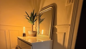 Een badkamer met een wit wastafelmeubel, een rond krukje, een spiegel en een potplant.