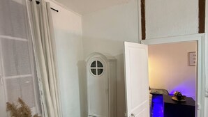 Een kamer met een houten vloer, een witte garderobe, een deur die leidt naar een andere kamer met een blauw verlicht gedeelte, en een plant met hoge, veerraamachtige bladeren.