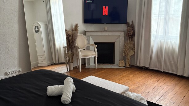 Een slaapkamer met een groot bed, een televisie boven een open haard en een spiegel aan de muur.