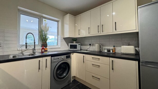 A modern kitchen with a washing machine, microwave, and stainless steel refrigerator.