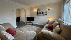 A living room with two beige sofas, a flat-screen TV, a small table, and a wall-mounted picture.