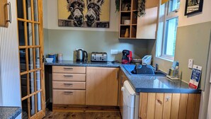A compact kitchen with wooden cabinets, a built-in dishwasher, and a countertop with a kettle, toaster, and coffee maker. - Cosy Annexe on The Isle of Skye. Family friendly, stunning vistas close to beach (Isle Of Skye)