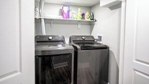 A laundry room with two front-loading washing machines and a shelf above containing various laundry supplies. - SAINT SUITES EXECUTIVE STAY 2B + 1B (Brampton)