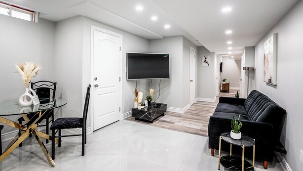 A modern living room with a glass dining table, black sofa, and a flat-screen TV mounted on the wall. - SAINT SUITES EXECUTIVE STAY 2B + 1B (Brampton)