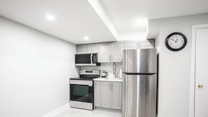 A modern kitchen with stainless steel appliances, white cabinetry, and a wall clock. - SAINT SUITES EXECUTIVE STAY 2B + 1B (Brampton)
