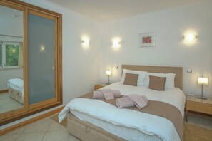 Una cama bien hecha con almohadas y una colcha, lámparas de noche, un espejo grande y un cuadro en la pared.